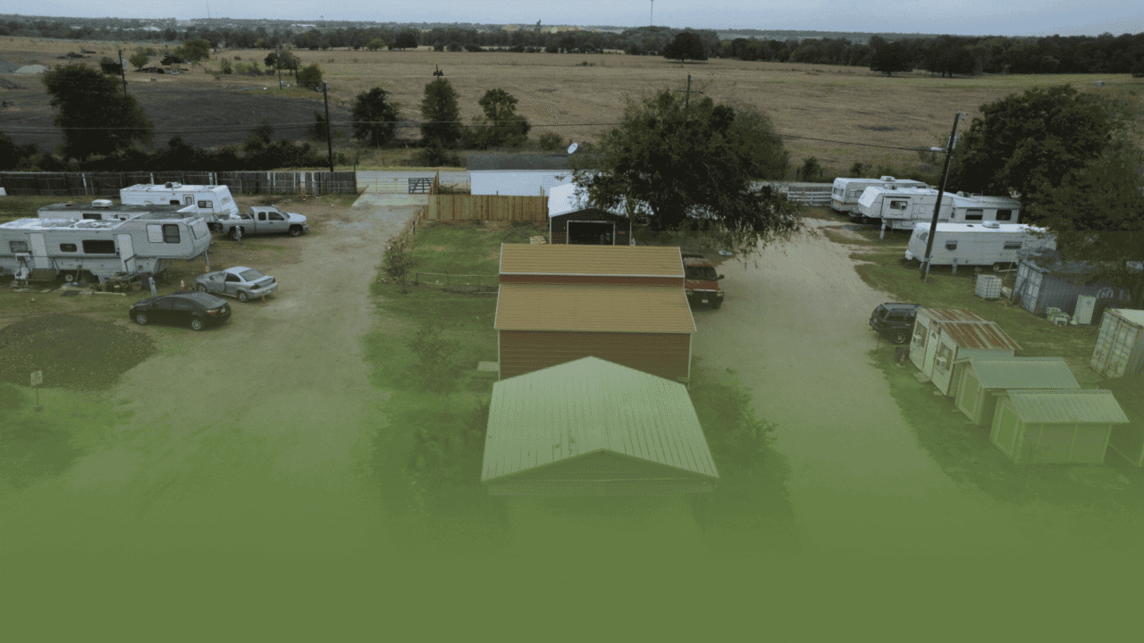 Aerial view of three buildings in a rural area with surrounding vehicles and trees.
